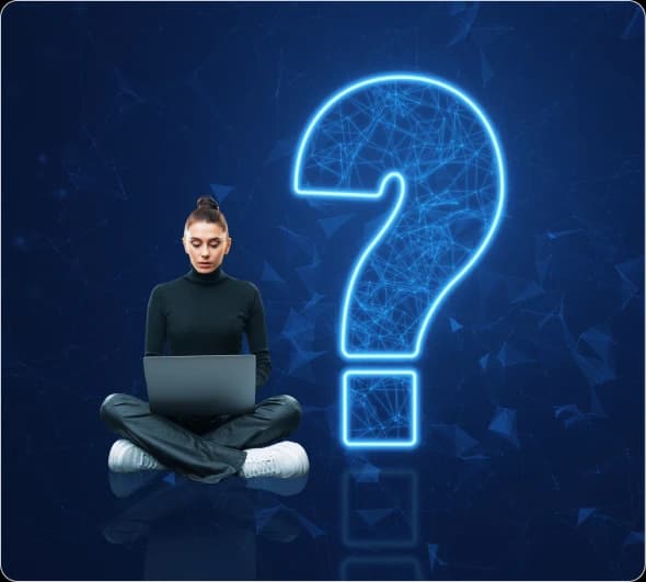 A person sitting cross-legged with a laptop beside a glowing neon question mark